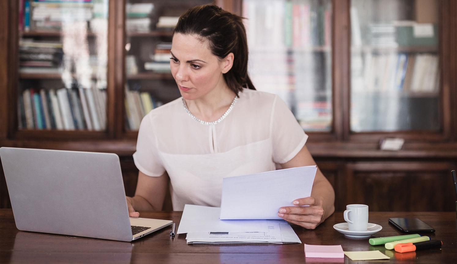 woman at dark wood desk with bookshelves behind her, using computer